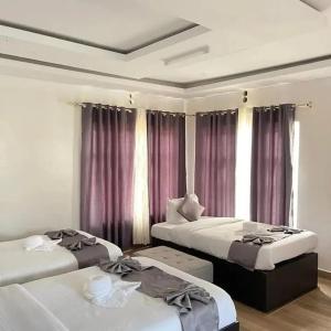 two beds in a room with purple curtains at MASAI MARA COTTAGES in Narok