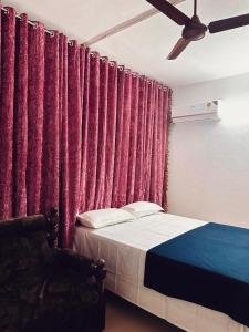 a bedroom with red curtains and a bed with a chair at Puthookkadans Mareena Lodge in Kottayam