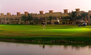 un homme debout sur un parcours de golf devant un bâtiment dans l'établissement Al Hamra Village Hotel, à Ras al Khaimah