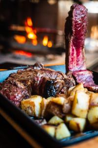 a plate of steak and potatoes in front of a fireplace at Al Fogolâr Rooms & Osteria with Saunaland in Tolmezzo