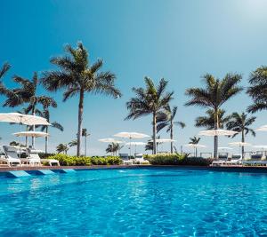 a swimming pool with palm trees and chairs and umbrellas at Grand Luxxe with free Golf in Nuevo Vallarta 