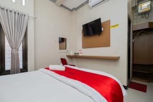 een slaapkamer met een rood en wit bed en een tv aan de muur bij RedDoorz near Kampung Inggris Pare in Pare