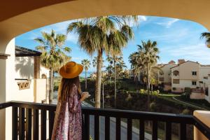 米哈斯科斯塔的住宿－Wyndham Grand Costa del Sol，站在一个眺望棕榈树的阳台的戴帽子的女人