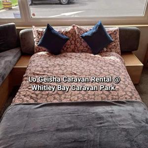 a bed with pillows on a couch with the words la gstaña caravan at Lo Geisha Caravan Rental at Whitley Bay Caravan Park in Whitley Bay