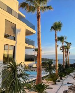 a building with palm trees next to a swimming pool at Primosten Resort Sunhill Deluxe Apartment Laura in Primošten