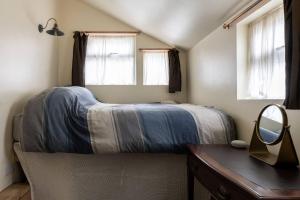 a bedroom with a bed and a desk and two windows at Adorable and Cosy Tiny Cottage in Heathfield
