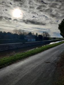 un camino vacío junto a un río con un cielo nublado en Le logis du pont, en Champagné-les-Marais