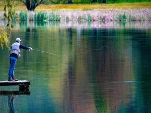 a man standing on a dock holding a fishing line in the water at Lake Naverone Holiday Cottages in Drakensberg Garden