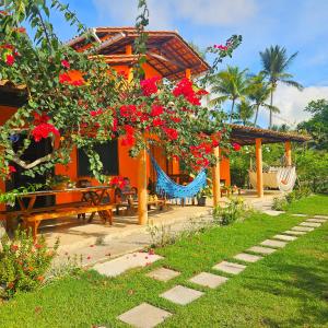 a house with a hammock and red flowers at Villa Mar a Vista - Suite Alamanda in Cumuruxatiba