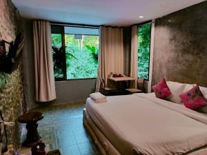 a bedroom with a bed and a table and a window at THANSILA Resort in Ranong