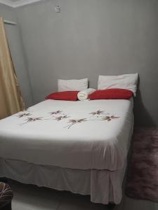 a bedroom with a bed with white sheets and red pillows at Partulaka Rest Inn in Maun