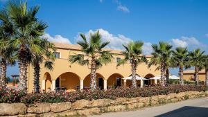 ein Gebäude mit Palmen und Blumen davor in der Unterkunft Hotel Donna Carmela Sede Unica a Sciacca in Sciacca