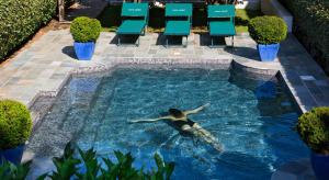 kobieta pływająca w basenie z krzesłami w obiekcie Demeure Castel Brando Hôtel & Spa w mieście Erbalunga