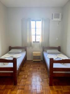 two beds in a small room with a window at Hotel Bandeirantes de SJBV in São João da Boa Vista