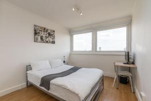a bedroom with a bed and a desk and two windows at City View Apartments - Bow in London