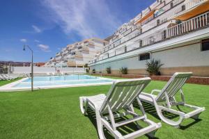 two chairs sitting on the grass next to a swimming pool at Bright Amadores Seaview Apartment in Puerto Rico de Gran Canaria