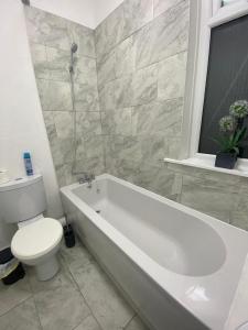 a bathroom with a white tub and a toilet and a window at Three En-Suit Rooms in Manchester