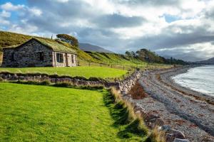 an old house with a grass roof next to the ocean at The Ruin - Lochside Cottage dog friendly in Ullapool