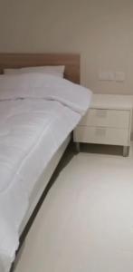 uma cama com lençóis brancos e uma mesa de cabeceira em Salalah Forest Island Villa em Ţāqah
