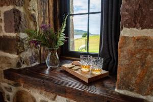 a window sill with two glasses and a vase of flowers at The Wreck - Lochside cottage Dog Friendly in Ullapool