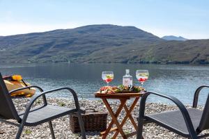 two glasses of wine sitting on a table next to a lake at The Wreck - Lochside cottage Dog Friendly in Ullapool