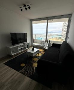 a living room with a black couch and a large window at Dpto en Resort Laguna del Mar frente al mar 2D2B in La Serena