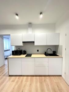 a kitchen with white cabinets and a wooden floor at Apartament SASANKA in Kudowa-Zdrój