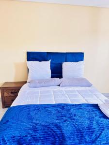 un letto con testiera blu e lenzuola e cuscini bianchi di Legae garden home a Gaborone