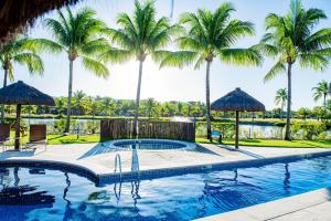 a swimming pool with umbrellas and palm trees at Condominio Iberostate in Praia do Forte