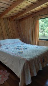 a bed in a log cabin with a window at Cabaña Río Iculpe in Lago Ranco