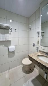 a white bathroom with a toilet and a sink at Cedro Hotel in Londrina