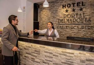 Un uomo e una donna in piedi al bancone di un hotel di El Portal Del Marques a Cajamarca