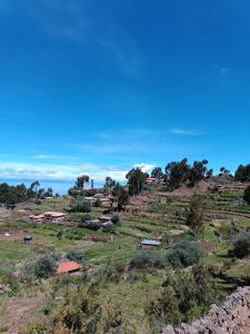 a view of a field with houses on a hill at Taquile Familia Celso in Huillanopampa