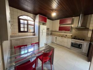 uma cozinha com uma mesa de vidro e cadeiras vermelhas em Casa confortável e espaçosa . em Florianópolis