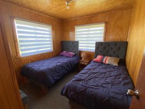 twee bedden in een kleine kamer met twee ramen bij Cabañas Los Queltehues in Chacao Viejo