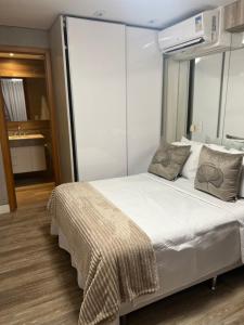 um quarto com uma cama grande com lençóis brancos e almofadas em Flat aconchegante no Jardim Goias em Goiânia