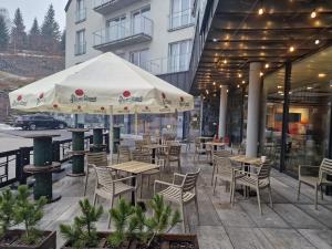 un patio al aire libre con mesas, sillas y una sombrilla en Aparthotel Czarna Góra 239 en Sienna