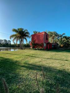 un edificio rojo en un campo con palmeras en Complejo Laguna Chica en Dique Luján