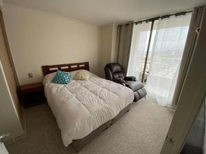 a bedroom with a bed and a chair and a window at Hermoso Departamento con excelente vista, a pasos de la Quinta Vergara, cercano a Reloj de Flores y Playa Caleta Abarca in Viña del Mar