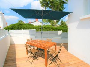 einen Holztisch mit Stühlen und einem Sonnenschirm auf einer Terrasse in der Unterkunft Maison La Tranche-sur-Mer, 3 pièces, 4 personnes - FR-1-22-322 in La Tranche-sur-Mer