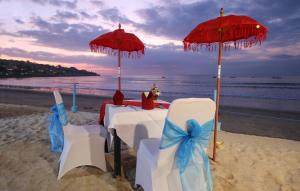 una mesa y sillas en una playa con sombrillas en Kupu Kupu Jimbaran Beach Hotel & Spa by L’Occitane en Jimbaran