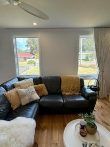 um sofá de couro preto numa sala de estar com duas janelas em Owl+Oak em Castlemaine