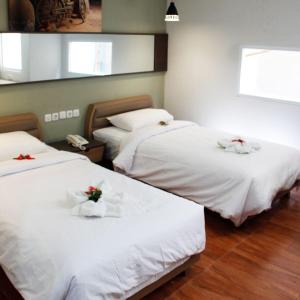 two beds in a room with white sheets and flowers on them at AZKA HOTEL Managed by Salak Hospitality in Jakarta