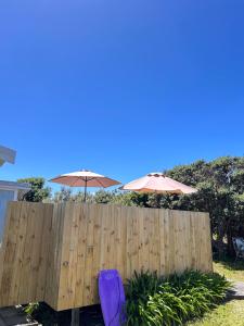 a wooden fence with two umbrellas and a purple chair at Kowhai Landing Beach Cabin in Otaki Beach +3 photos
