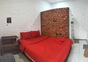 a bedroom with a red bed with a brick wall at AZALEA GARDEN HOMESTAY in Pagaralam