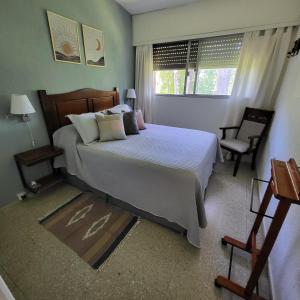 a bedroom with a bed and a chair and a window at Apartamento en Complejo Arcobaleno in Punta del Este