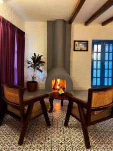 a living room with a fireplace with two chairs and a table at Aphrodite Homestays Coorg by The Almanac in Napoklu