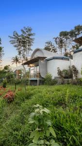 a house in a field of grass with a building at Aphrodite Homestays Coorg by The Almanac in Napoklu