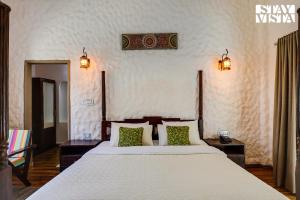a bedroom with a large white bed with green pillows at StayVista's Bhils Kabeela - Kanha - Outdoor Pool, Games Room & Kids Zone in Kānha