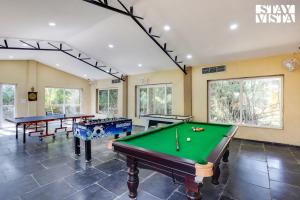 una sala de piscina con varias mesas y ventanas en StayVista's Bhils Kabeela - Kanha - Outdoor Pool, Games Room & Kids Zone en Dhanwār